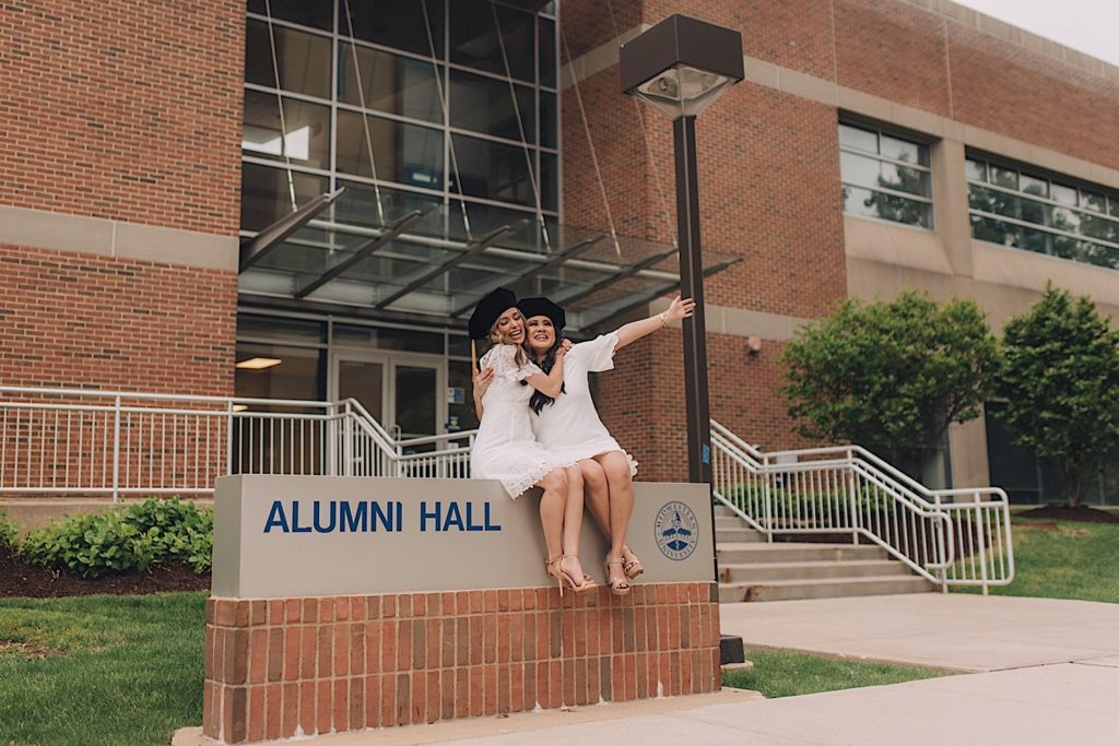 Friends sit atop Midwestern University's alumni hall sign for graduation session