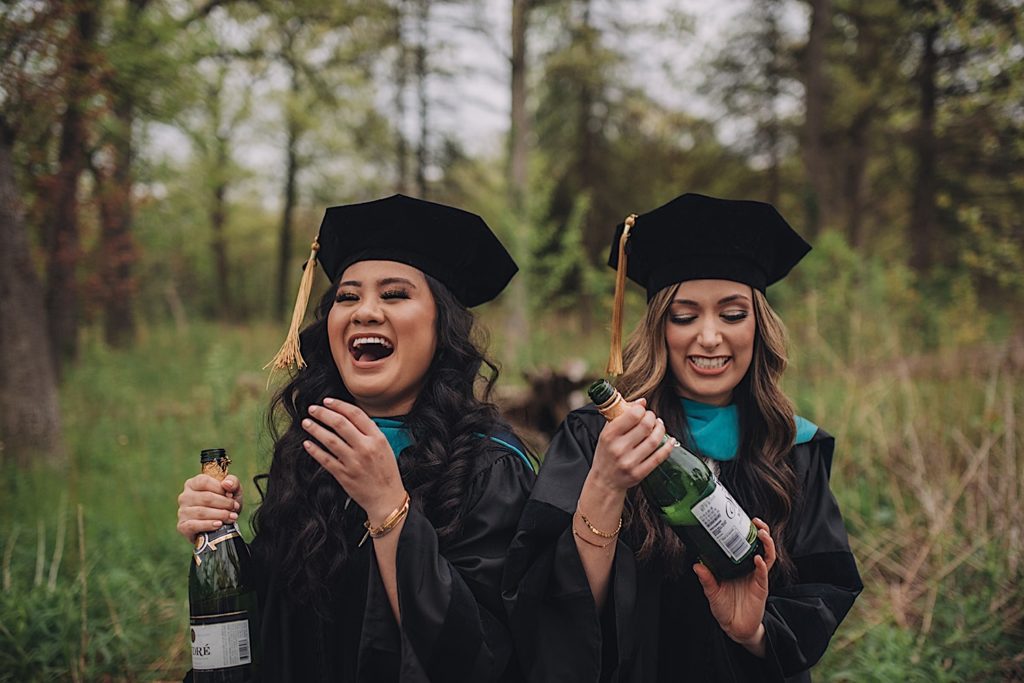 Friends hold bottles of champagne and grape juice during graduation session